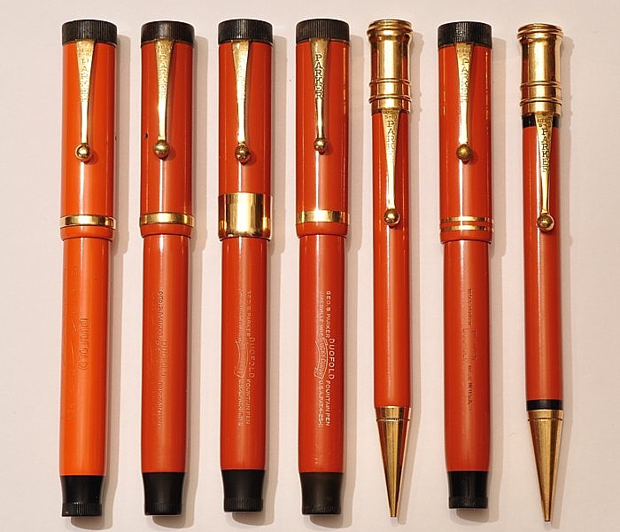 Parker Duofold &quot;Big Red&quot;. Von links: recht fühes Exemplar aus (hellerem) Hartgummi (1923), dunkleres Hartgummi (1924 - 25), &quot;De Luxe&quot; aus Zelluloid (1925), Zelluloid mit breitem Kappenband (1926 - 27), zugehöriger Bleistift, letzte Version der &quot;Flat Tops&quot; mit zwei Kappenbändern (1928) mit Bleistift.