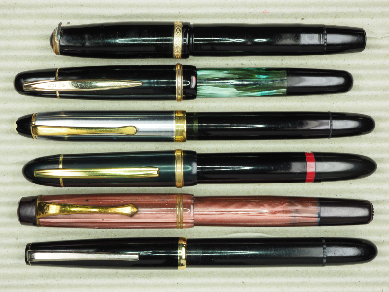 Tintenkugelschreiber (von oben): PAN, mit korrodiertem Clip; UHU Kugeltinter, 2. Generation; Montblanc-Simplo 444, verbesserte Version; Riepe GmbH Rollkuli, 2. Generation; Sphinx Rubidor; Roulette Diamant 55, mit fremder Kappe